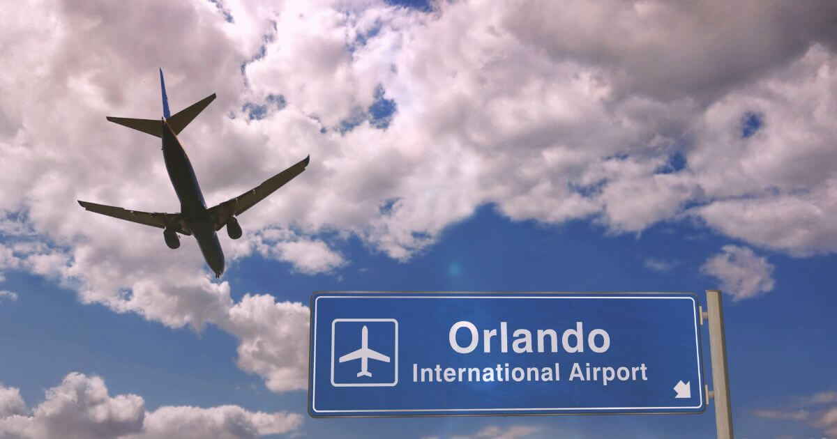 Horizontal photo of a plane flying over a sign that says Orlando International Airport.