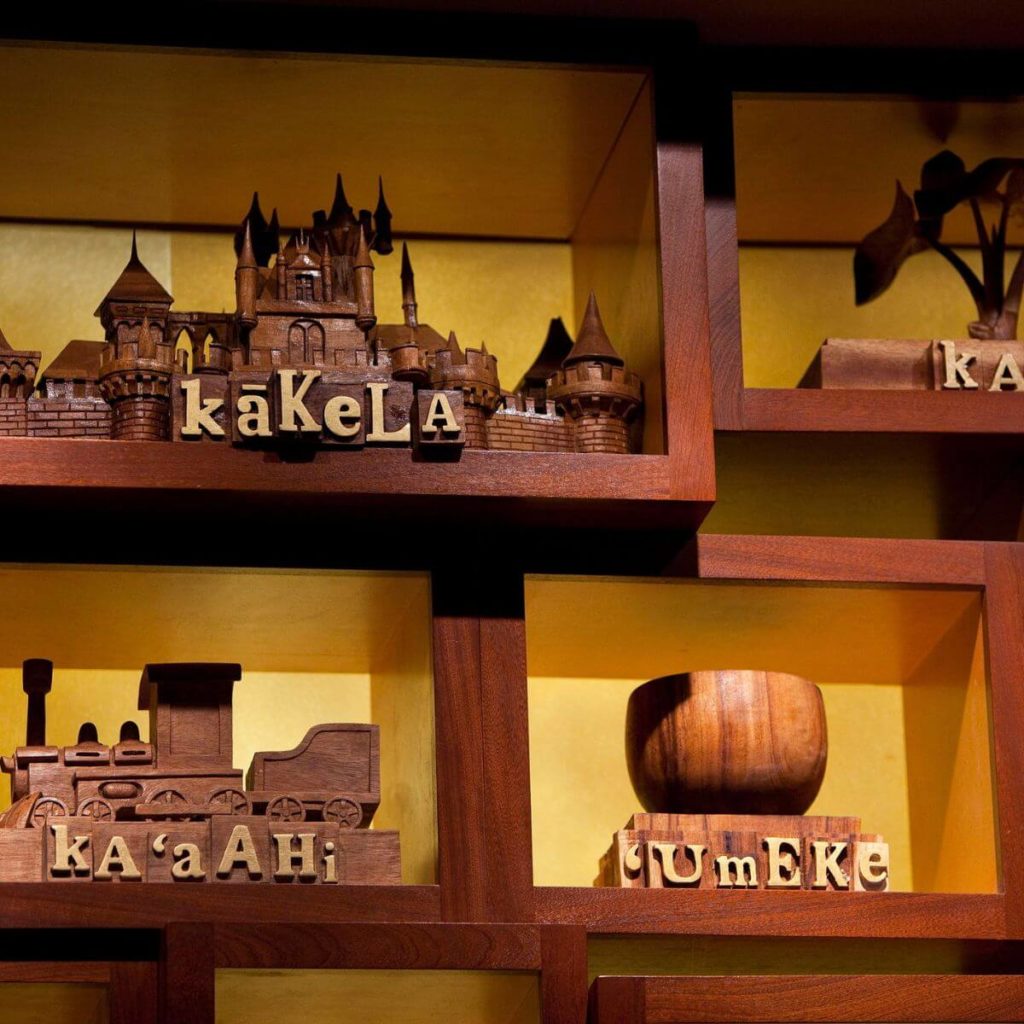 Closeup photo of wooden carvings, such as a castle and a train, with their Hawaiian word underneath them, at The 'Ōlelo Room at Aulani Disney Resort.