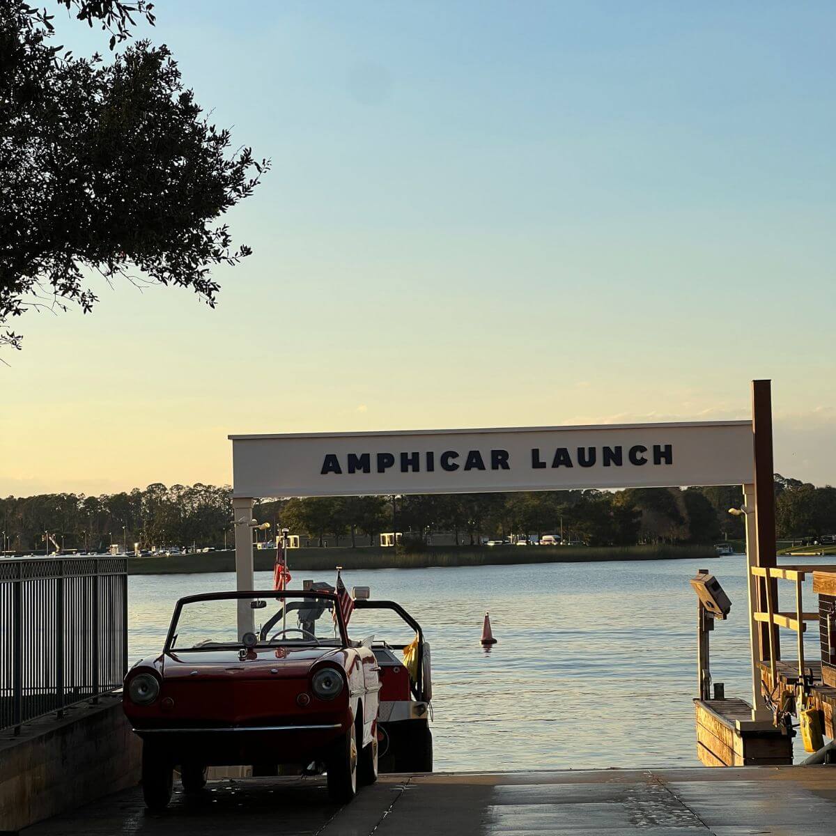 Photo of vintage amphicars parked at a dock that says "Amphicar Launch" on a banner.
