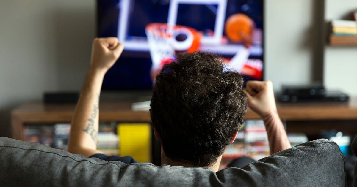 Photo of a man watching a basketball game on tv.