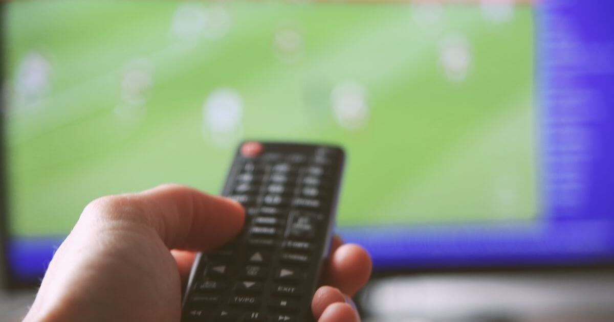 Photo of a person holding a tv remote pointing to a tv with a football game on.