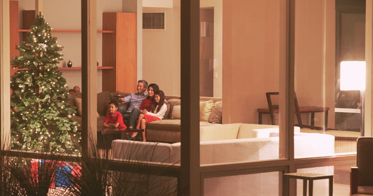 Photo of a family of 4 sitting on the couch with a Christmas tree nearby. Dad is holding up a tv remote.