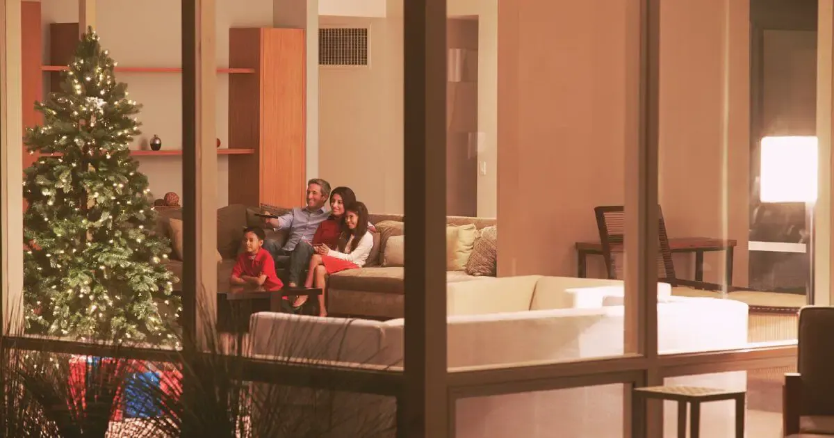 Photo of a family of 4 sitting on the couch with a Christmas tree nearby. Dad is holding up a tv remote.