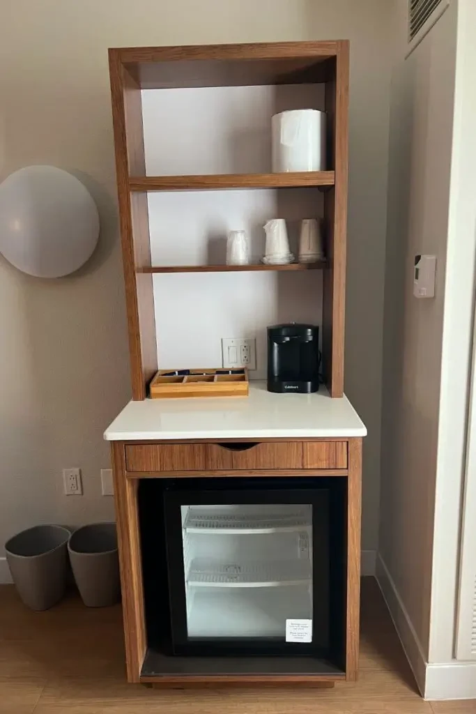 Photo of the drink station inside the Pop Century rooms with a mini refrigerator, coffee maker, cups, and shelf space.