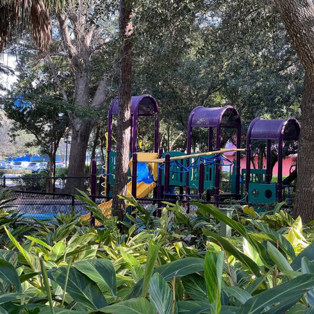 Photo of a playground with a slide and jungle gym in a shaded area.