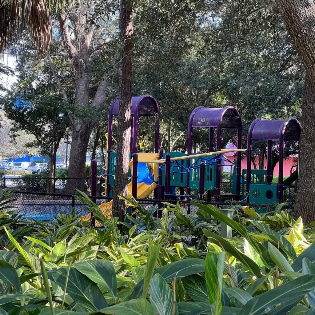 Photo of a playground with a slide and jungle gym in a shaded area.
