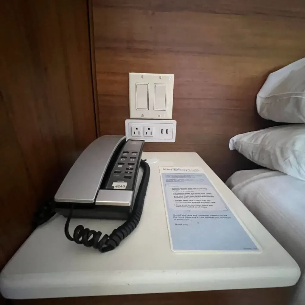 Closeup photo of a hotel room phone and outlets next to a bed.