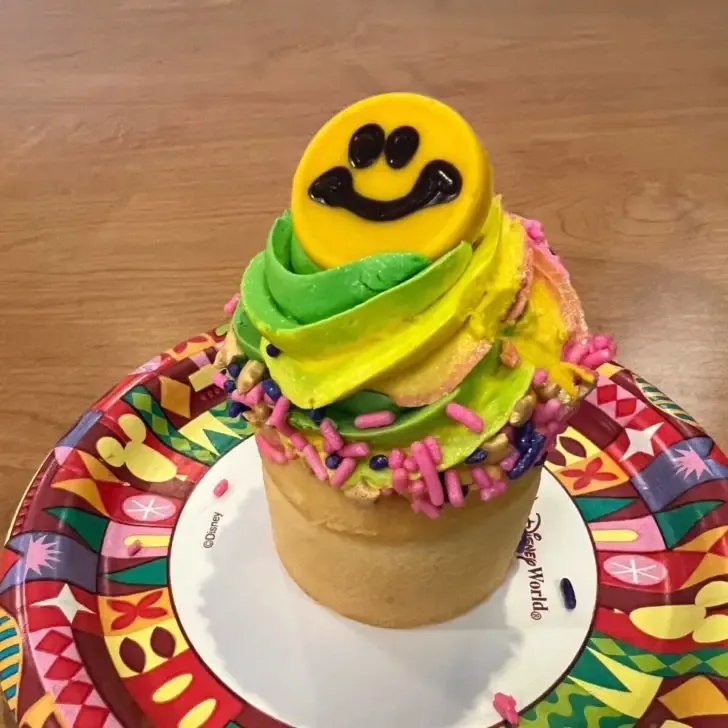 Photo of the POP Goes Banana Cupcake with tie dye frosting and a smiley face candy on top.