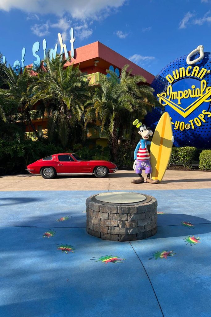 Photo of the campfire circle and a Goofy statue with a surfboard and vintage care at Disney's Pop Century Resort.