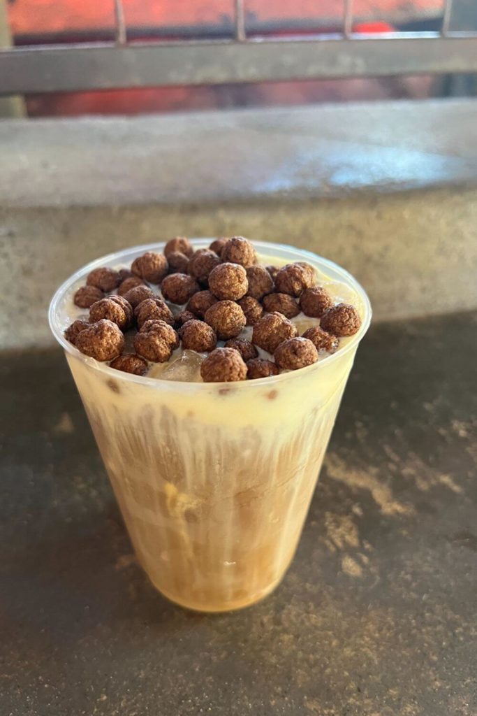 Photo of a black caf cold brew iced coffee with cocoa puffs on top.