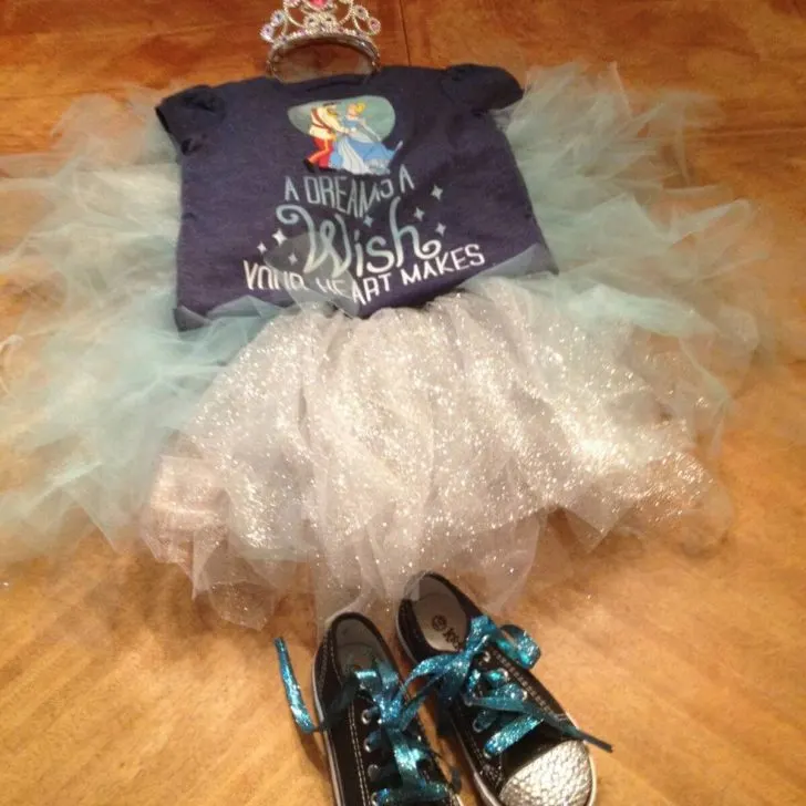 Photo of a crown, Cinderella t-shirt, blue and silver tutu, and black converse sneakers with rhinestones on the toe box.