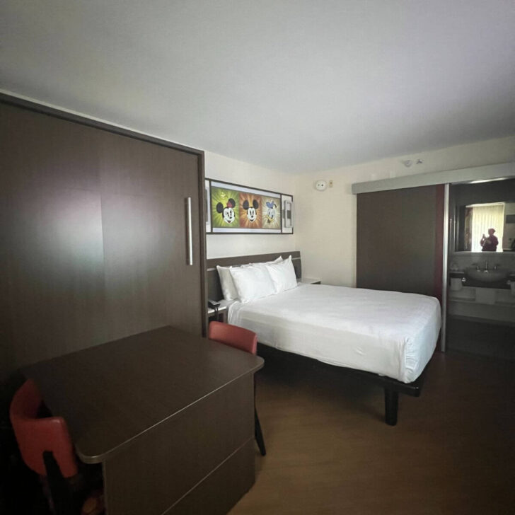 Photo of the Disney All-Star Movies Resort rooms with 1 queen bed and 1 queen murphy bed closed to expose a table and 2 chairs.