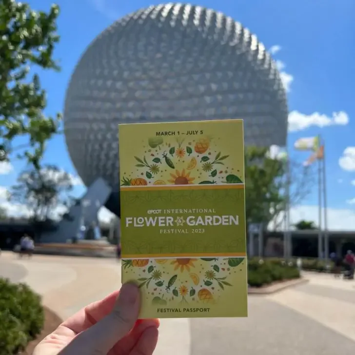 Photo of an Epcot International Flower & Garden Festival passport held up in front of Spaceship Earth.