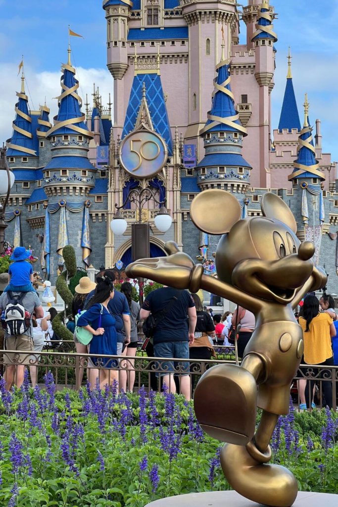 Photo of the golden Mickey Mouse statue in front of Cinderella's Castle at Walt Disney World's Magic Kingdom.
