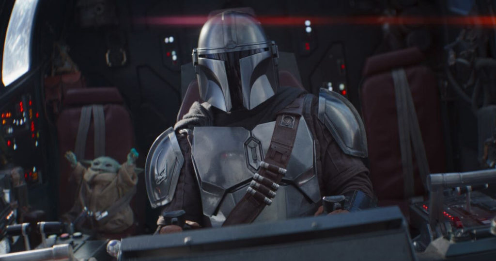 Photo still from season 2 of The Mandalorian featuring Mando flying his ship while Grogu cheers in the background while eating a blue macaron.