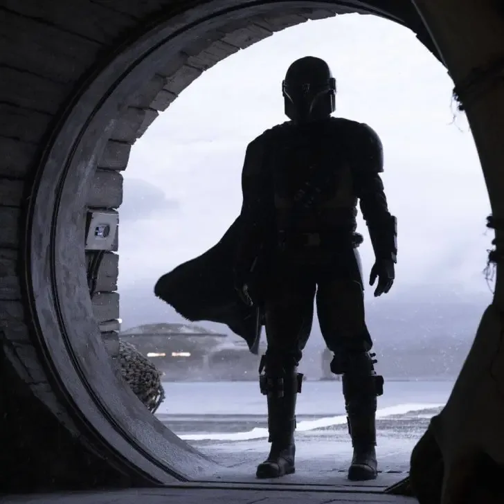 Photo from the opening scene of season 1 of Lucasfilm's The Mandalorian, showing the titular character, played by Pedro Pascal, in a round opening of a building.