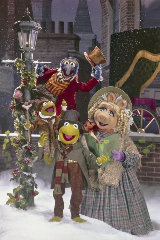 Photo still from the Disney Christmas movie, The Muppets Christmas Carol, with Gonzo, Kermit, Miss Piggy, and Tiny Tim posing on a snowy street.