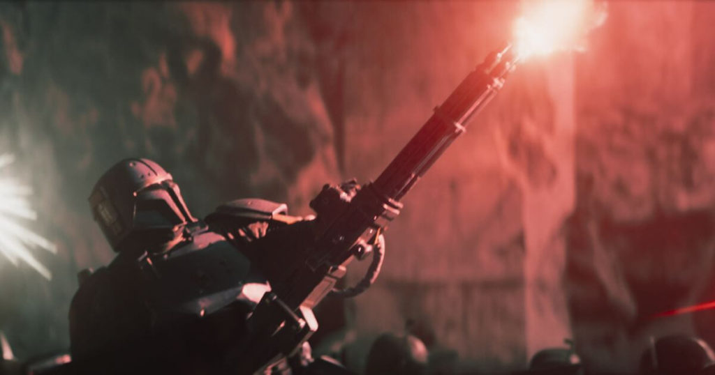 Photo still of a scene featuring Tait Fletcher as Paz Vizsla as he shoots a massive gun in a battle against stormtroopers.