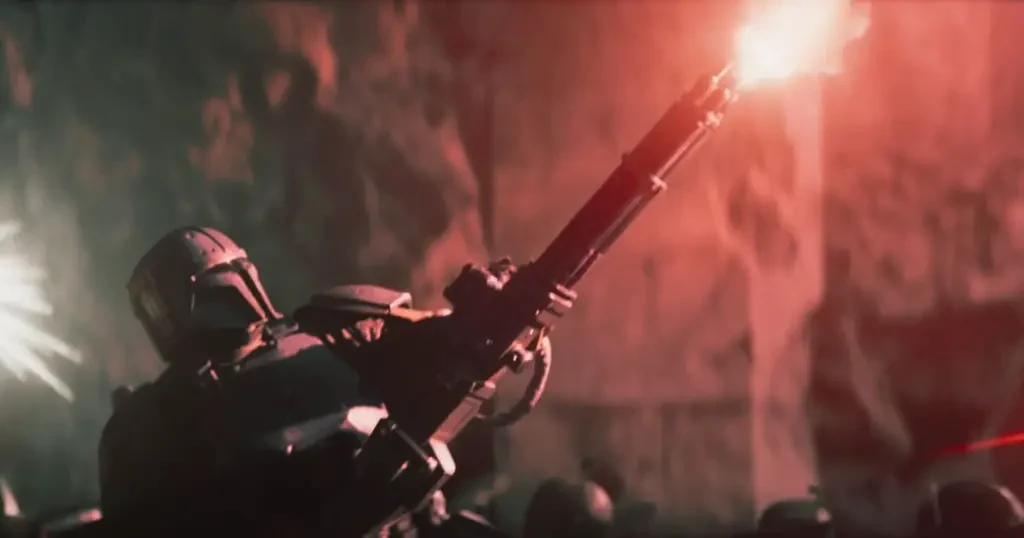 Photo still of a scene featuring Tait Fletcher as Paz Vizsla as he shoots a massive gun in a battle against stormtroopers.