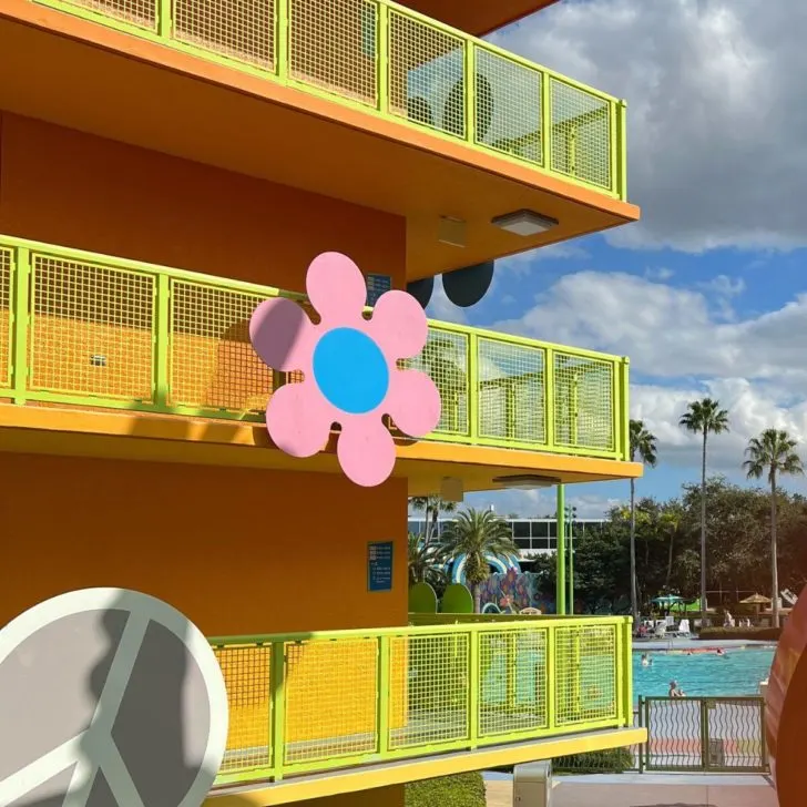 Photo of the exterior of the Pop Century Resort with groovy flowers and a peace sign on the railing and the pool in the background.