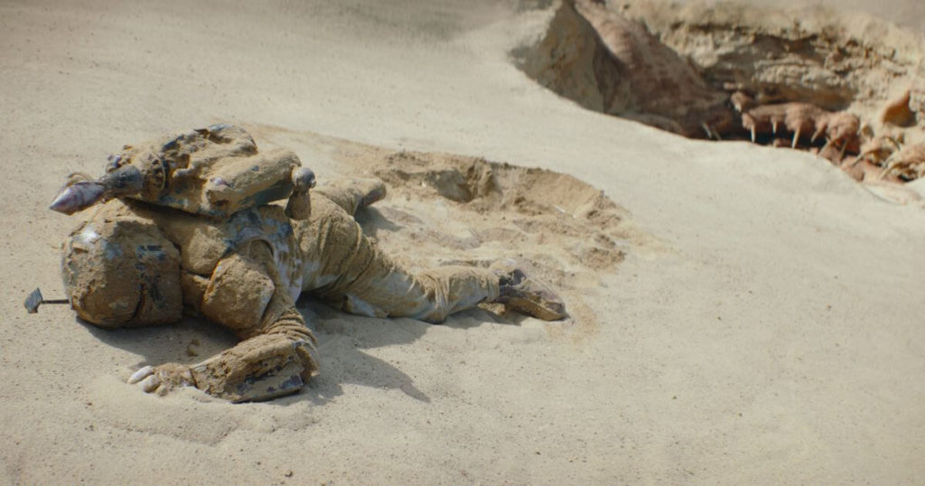 Photo still of Boba Fett as he is crawling out of the sands of Tatooine.