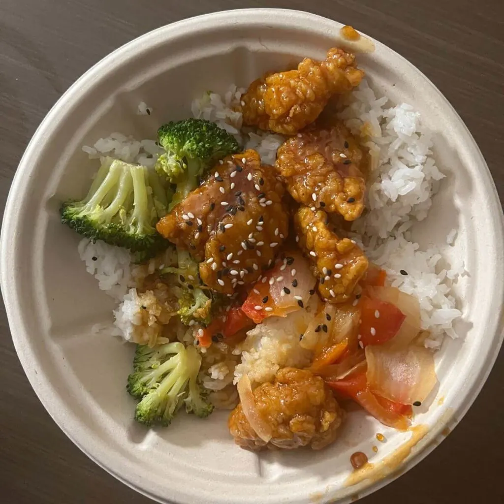 Top-down photo of a bowl filled with jasmine rice, broccoli, peppers, and sesame crispy chicken.