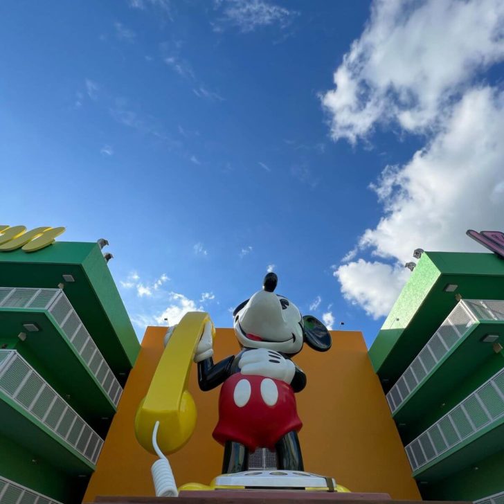 Photo of a massive statue of Mickey Mouse holding a yellow rotary phone with hotel room buildings on each side.