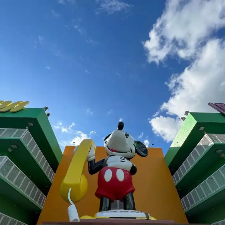 Photo of a massive statue of Mickey Mouse holding a yellow rotary phone with hotel room buildings on each side.