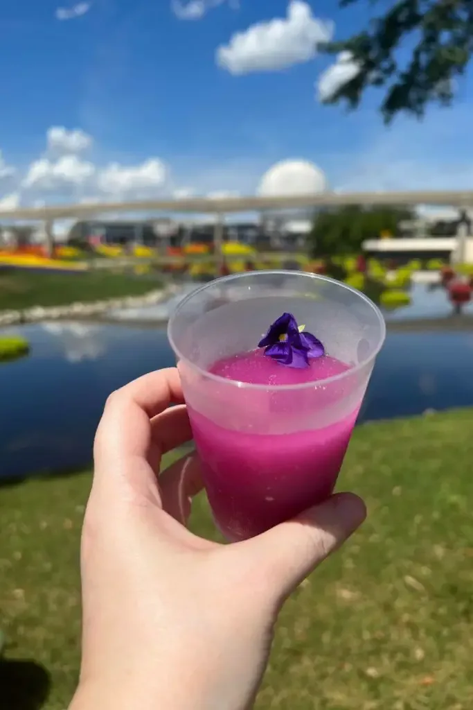 Photo of a glass of frozen violet lemonade held up in front of the Epcot Spaceship Earth ball.
