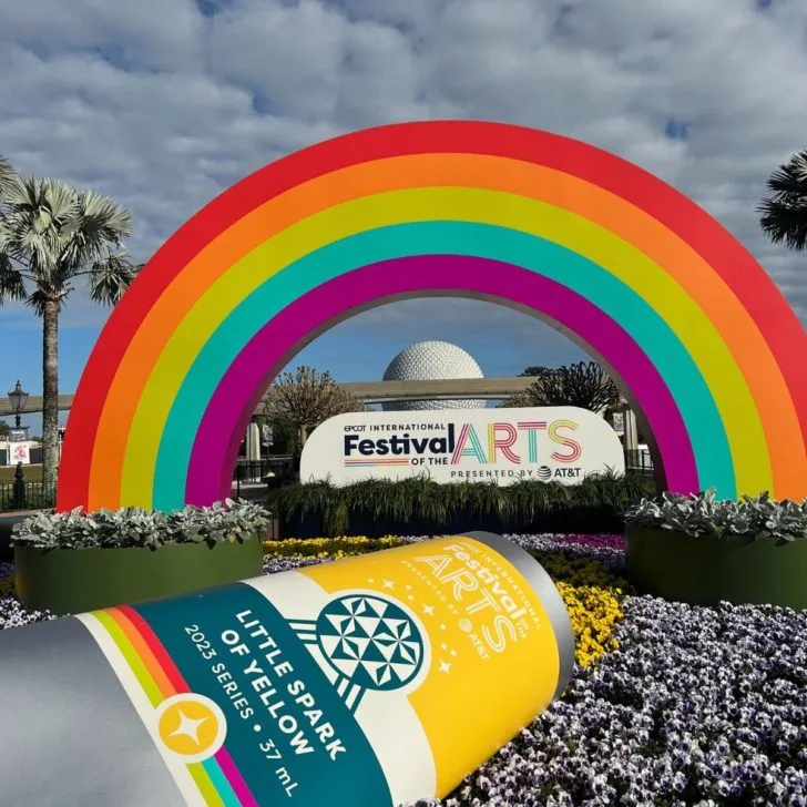 Photo of signage for the Epcot International Festival of the Arts with a fake paint tube and a giant rainbow with Spaceship Earth in the background.