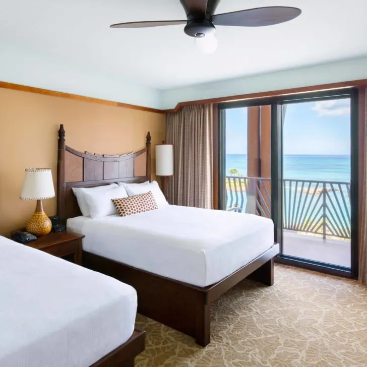 Photo of a standard room with an ocean view at Aulani, with 2 queen beds and a balcony overlooking the lagoon.