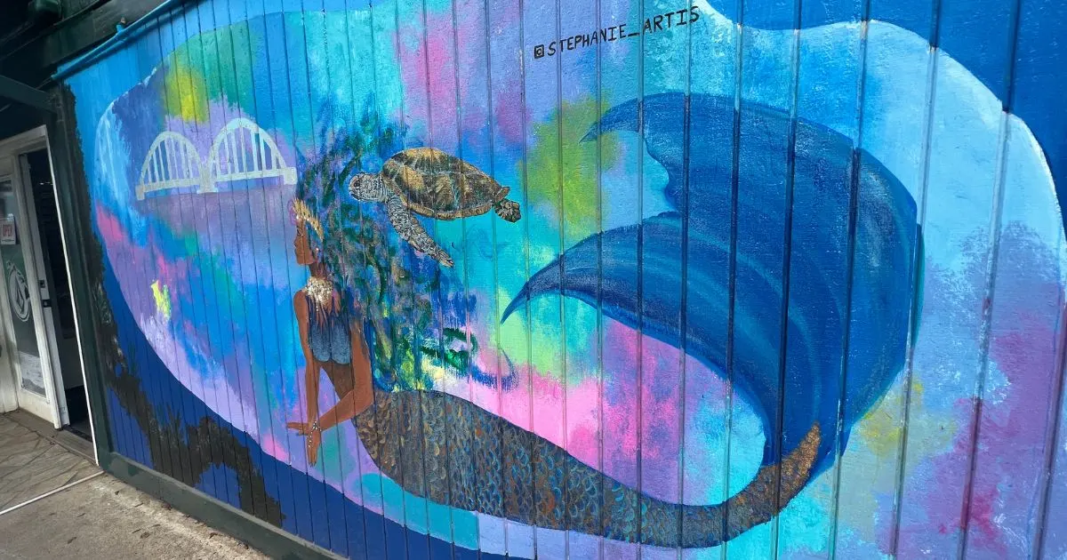 Photo of a massive mural by Stephanie Artis on the side of a store in Haleiwa, HI featuring a black mermaid and a sea turtle.