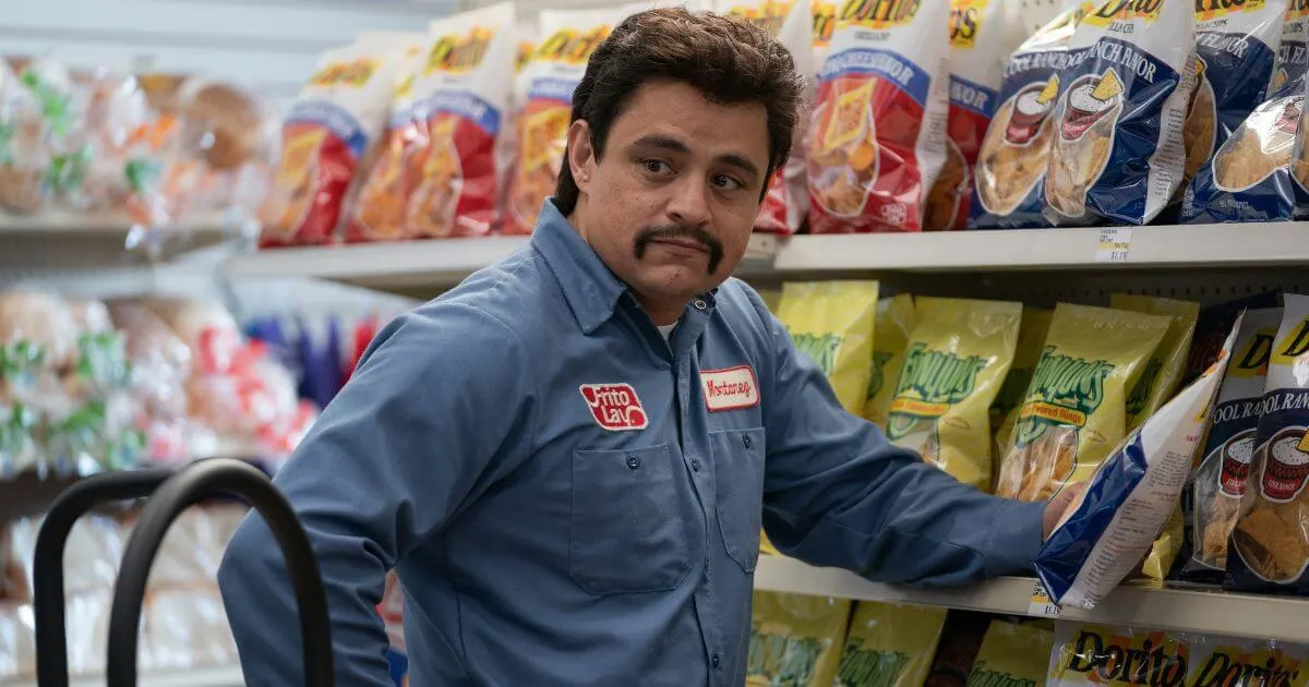 Photo still from the movie Flamin' Hot with Jesse Garcia next to shelves packed with chips.