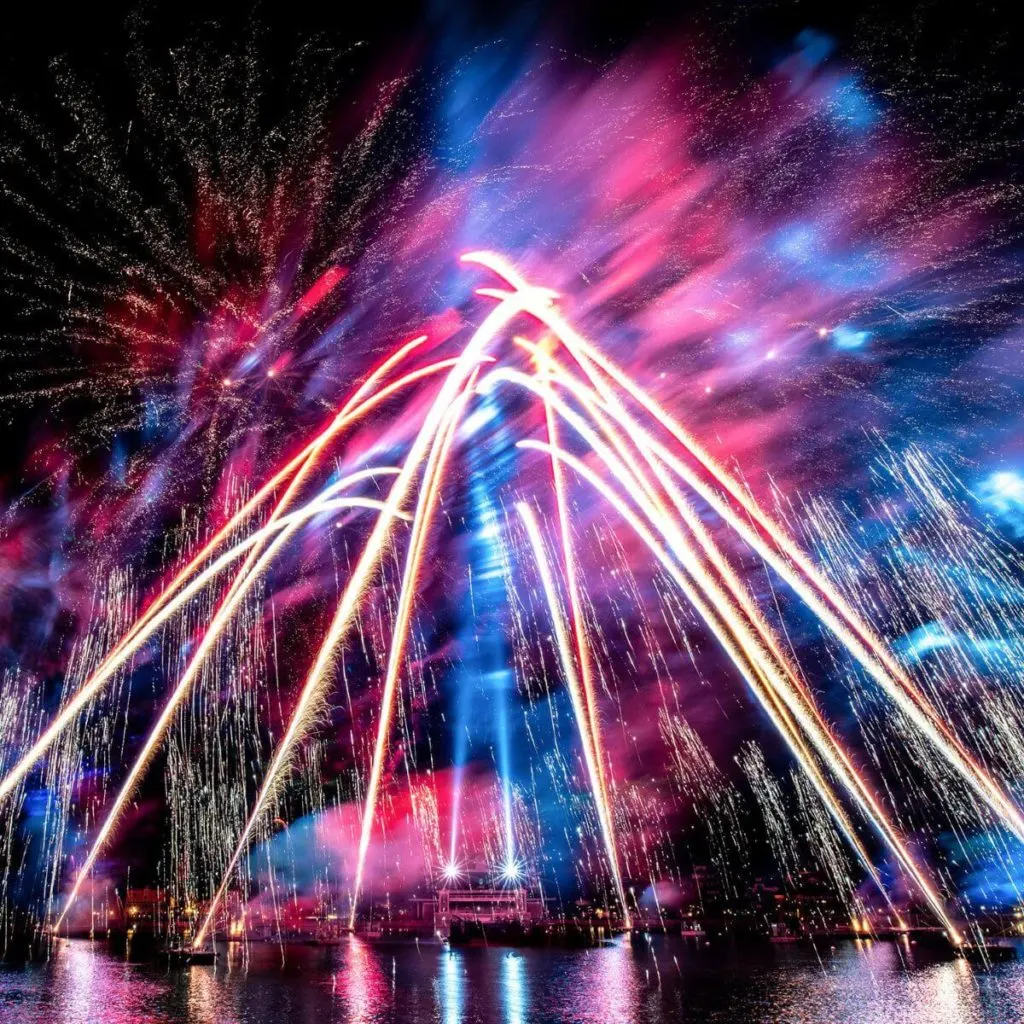 Photo of the Epcot Forever nighttime show with pink and blue lights and white fireworks.