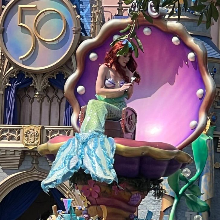 Photo of Ariel in mermaid form, sitting in a clamshell shaped chair on a float during the Festival of Fantasy Parade at Magic Kingdom.