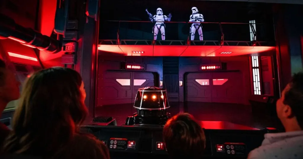 Photo from behind guests on a ride pod looking up to 2 stormtroopers watching them from a balcony.