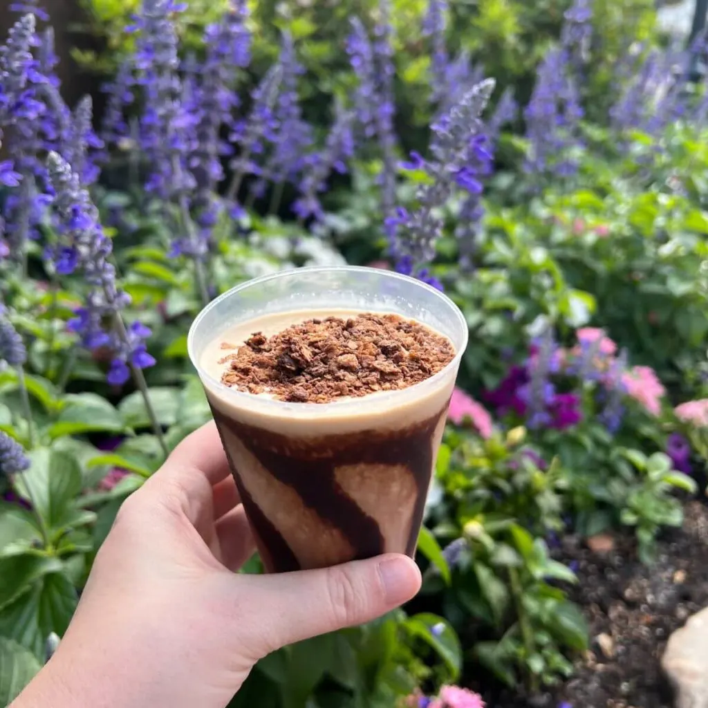 Photo of a cup of frozen viking coffee held up in front of purple flowers.