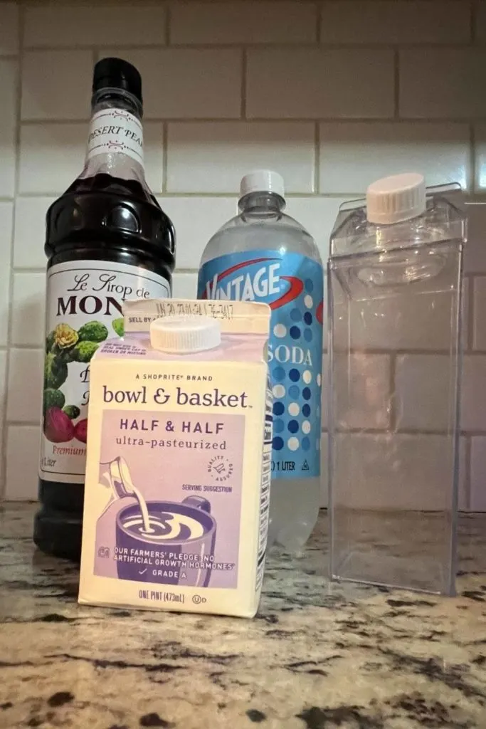 Photo of all the ingredients for a Milky Fizz Sipper drink: desert pear syrup, club soda, half & half, and a tall glass.