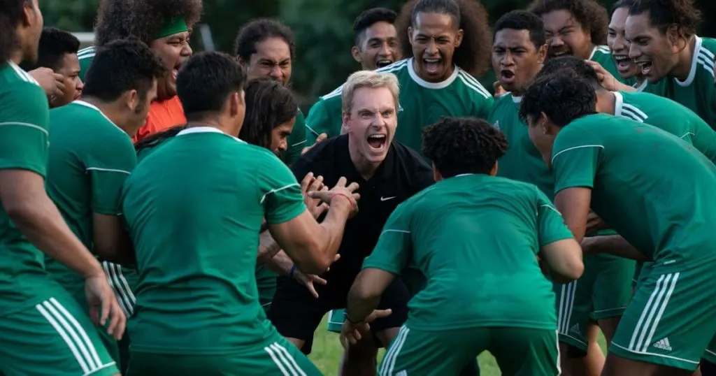 Photo still from the film, Next Goal Wins, showing the coach surrounded by his players.