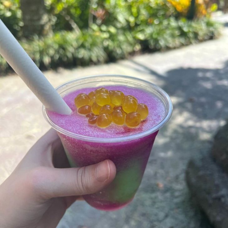 Closeup of a violet and green Night Blossom slushy with passion fruit boba on top and a thick straw.