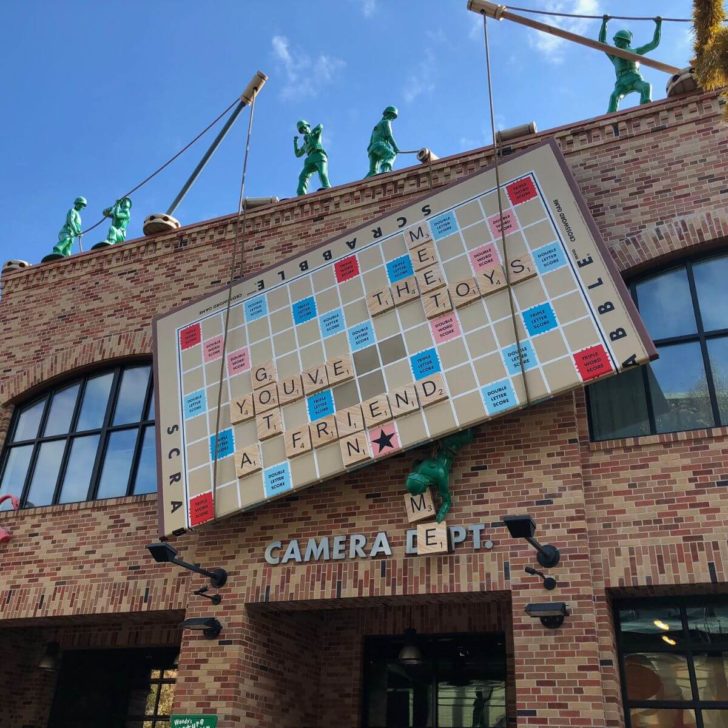 Photo of a building in Pixar Place with fake Green Army Men hoisting a Scrabble board to the top.