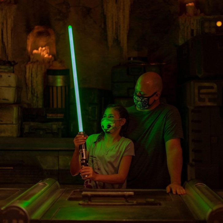 Photo of a young girl holding a blue lightsaber and a man at Savi's Workshop in Hollywood Studios.