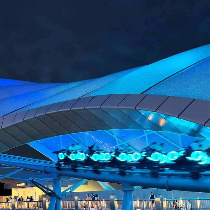 Photo of people zooming by on TRON at night, with everything lit up in blue.