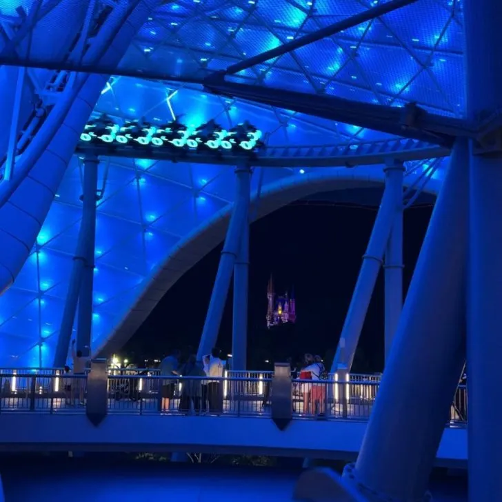 Photo of TRON Lightcycle Run lit up in blue at night with Cinderella's Castle in the background.