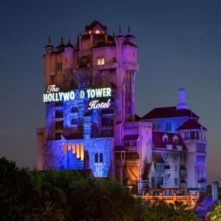 Photo of the Twilight Zone® Tower of Terror building in Hollywood Studios at night, with the front lit up in a purple-blue tone.