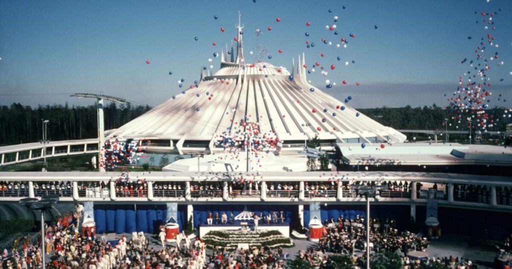 Photo of Space Mountain at Disney World's Magic Kingdom on opening day with red, white, and blue balloons falling in the sky and a crowd of people in the foreground.