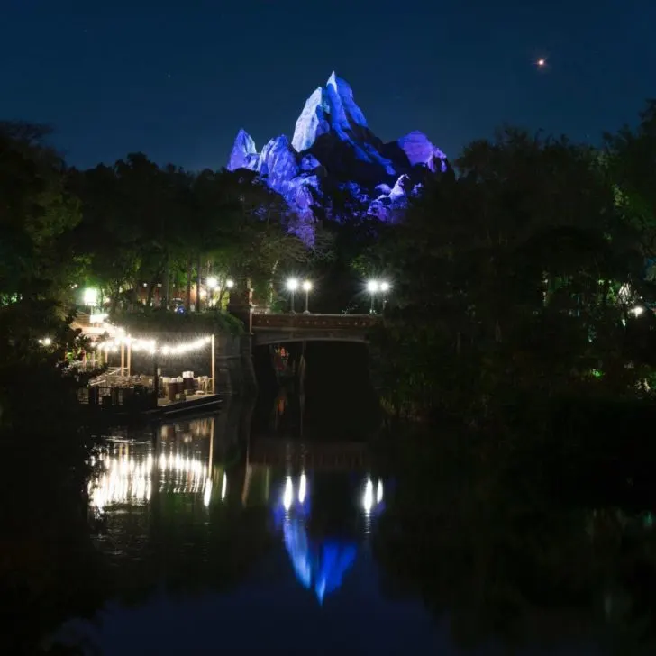 Photo of Expedition Everest mountain at night, reflecting in a river in the forefront.
