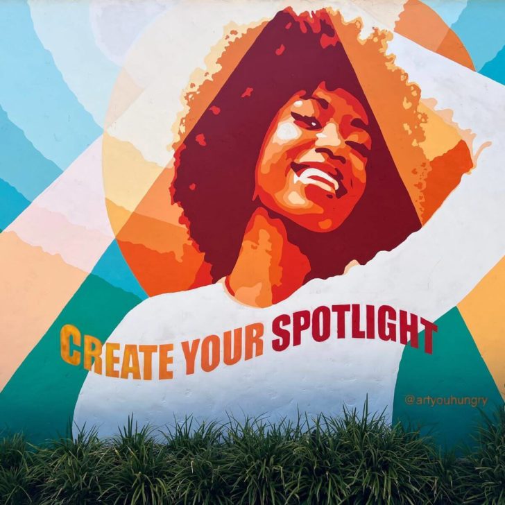 Photo of a street mural painting of a young woman with text that says "create your spotlight."
