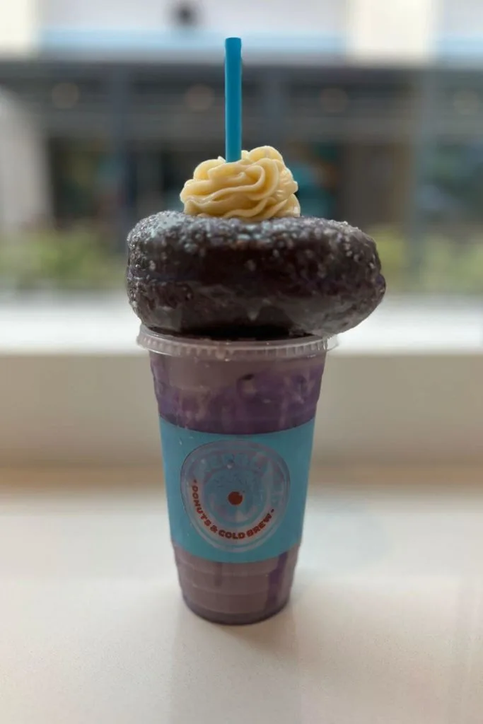 Photo of a purple ube donut on top of an iced ube chai latte from Everglazed Donuts & Cold Brew.