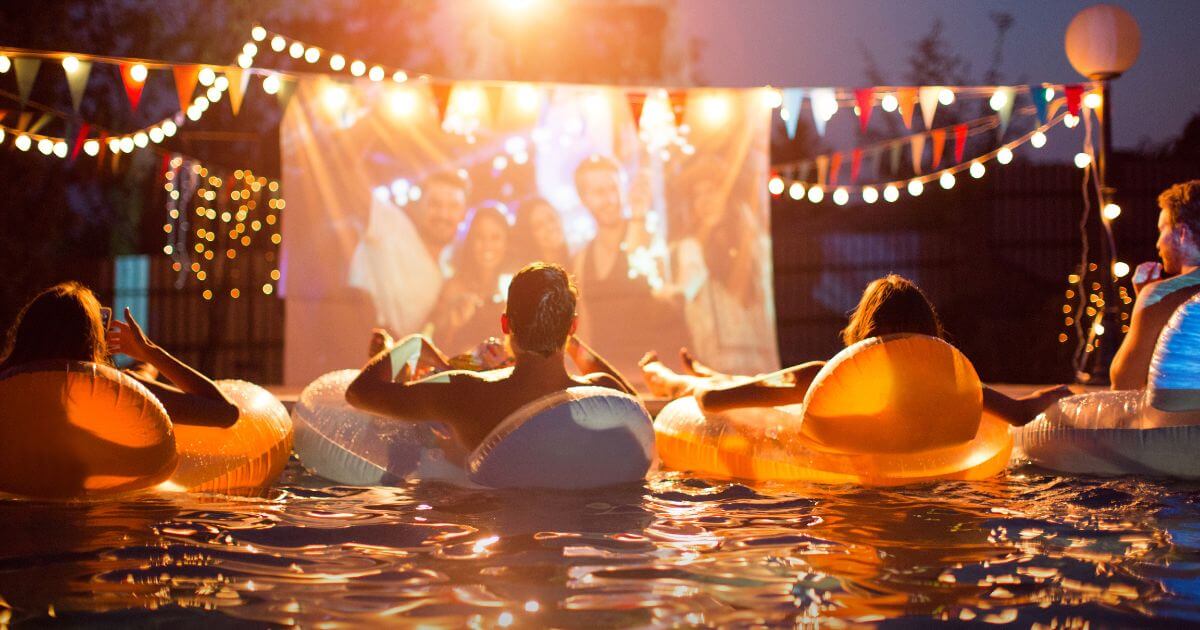 Photo of people sitting in floats in a pool while watching a movie projected on a large screen surrounded by patriotic decorations.